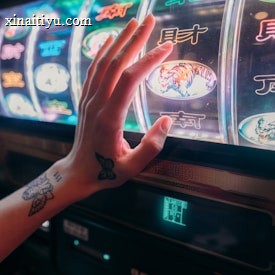 A hand with tattoos reaches towards a brightly lit slot machine, featuring various colorful symbols including a tiger. The image captures the moment of anticipation as the person engages with the machine during a game of chance.